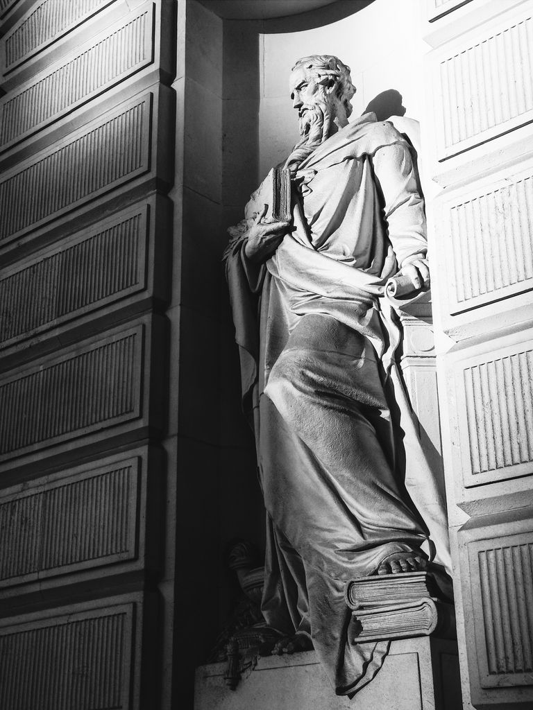 Black and white photo of a classical statue holding books, representing wisdom.